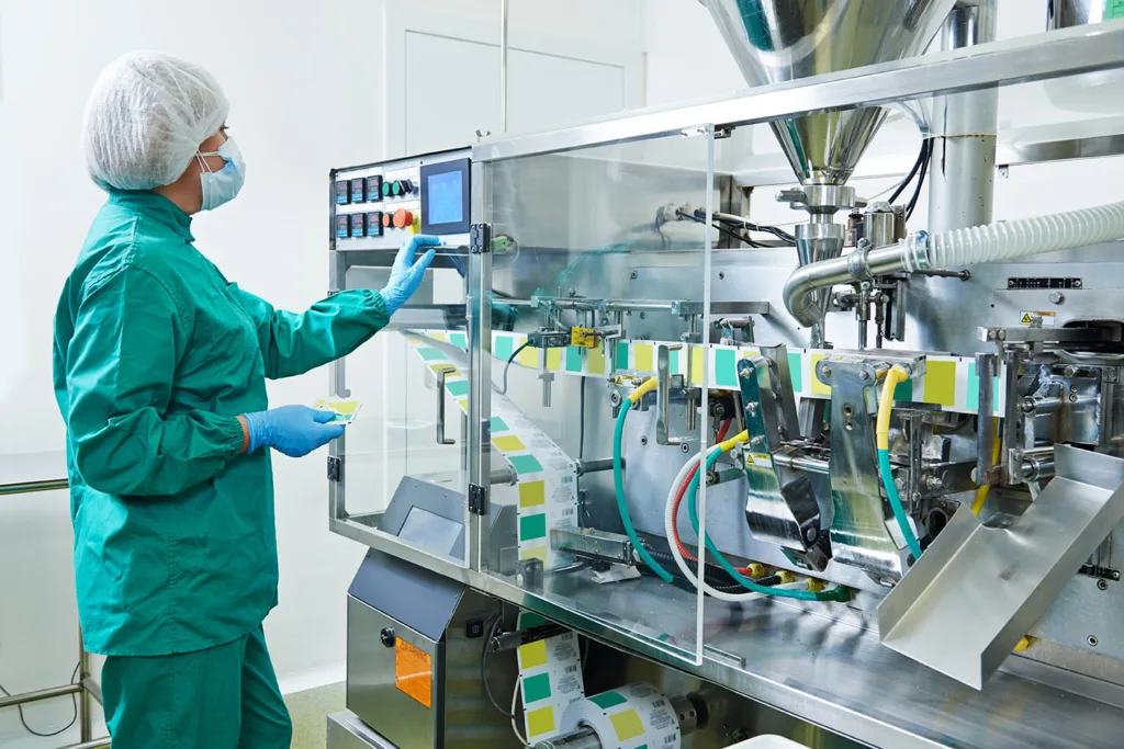 Operator obsługuje dotykowy panel HMI maszyny pakującej w czystej strefie produkcyjnej